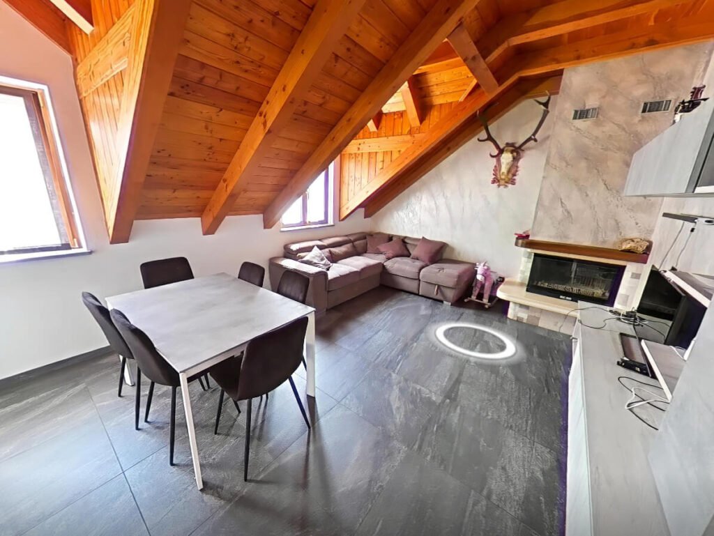 Zona giorno mansarda in montagna con travi a vista e camino, virtual tour immobiliare